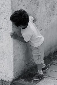 BOY LOOKING AROUND THE CORNER OF A BUILDING